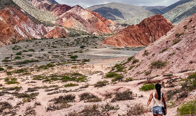 alt="Girl Carrying Camera And Walking Across the Paseo de Los Colorados Multi Coloured Mountains"